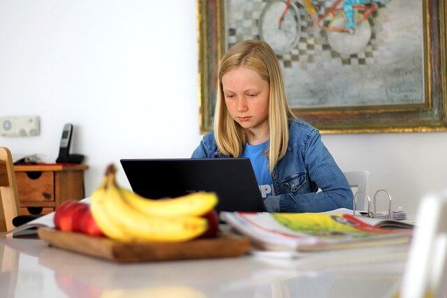 Fifth grade girl sitting at a table at home, working on her laptop