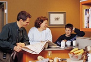 family at table doing school work and reading the newspaper