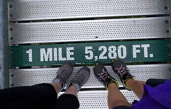 two pairs of feet standing on a sign that reads 1 MILE - 5280 Ft.